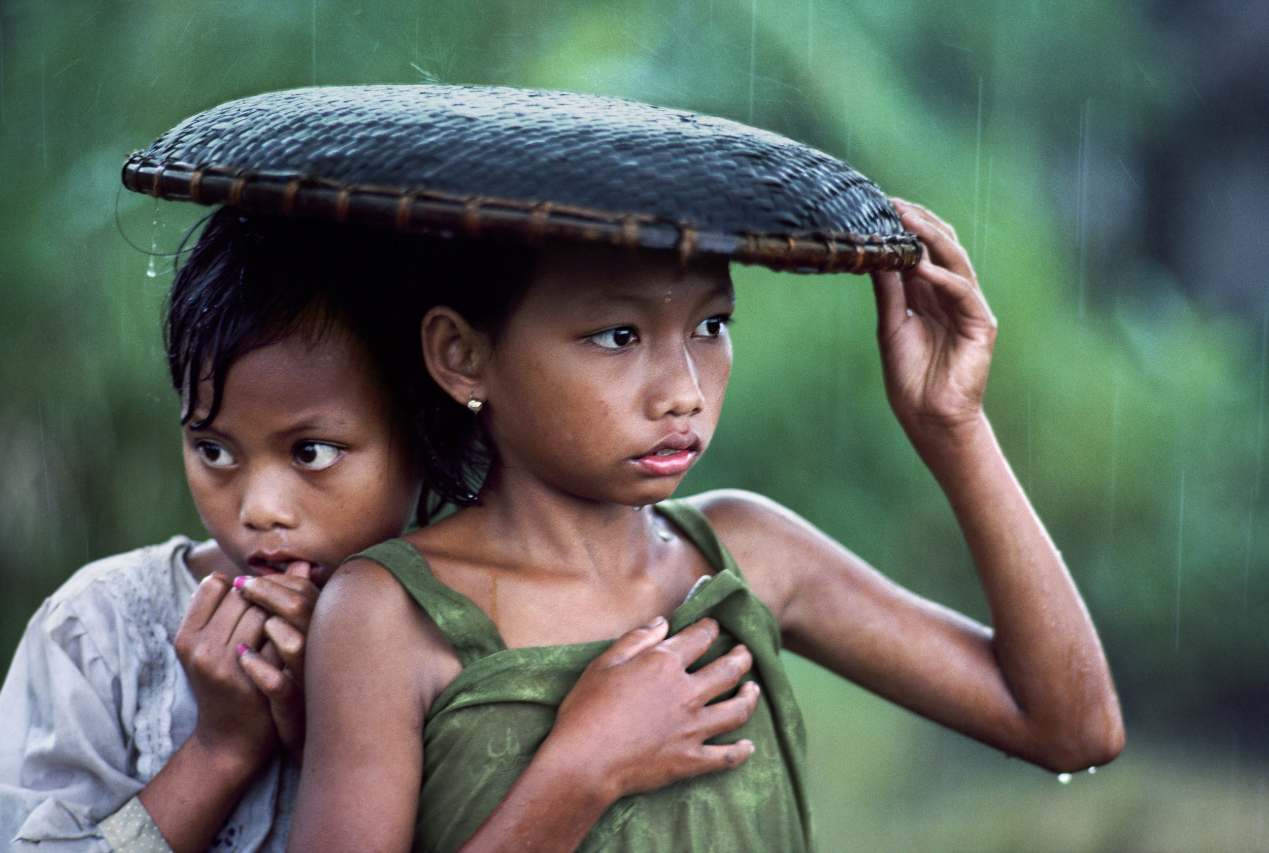 INDONESIA. Java. 1983. Girls huddle under a rice basket to escape the rain.